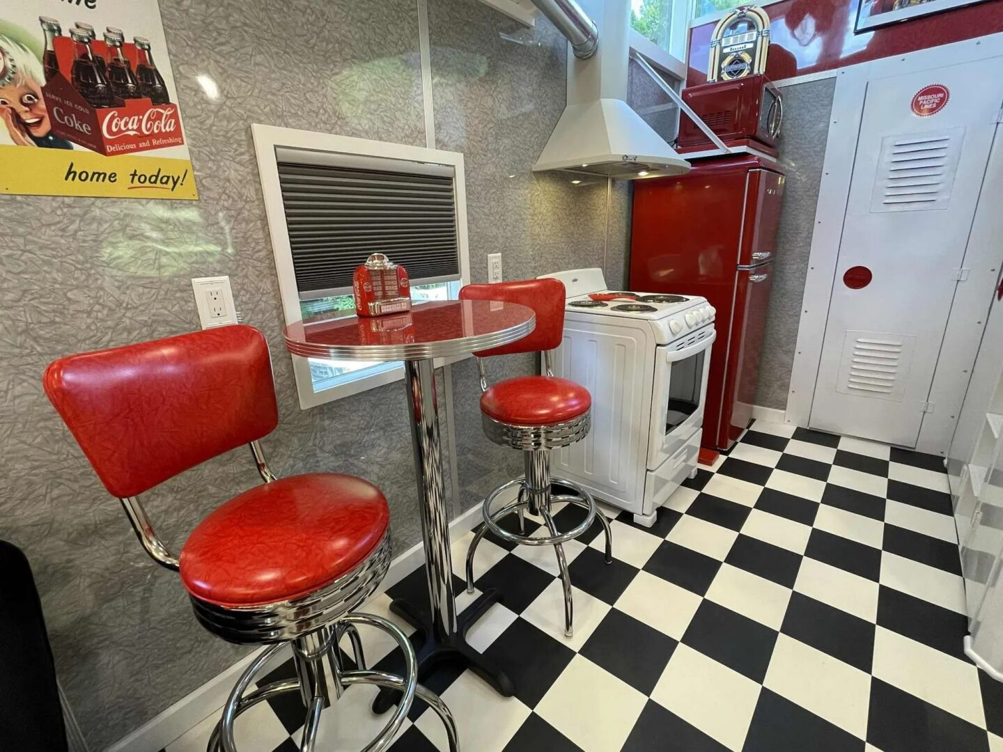 Retro diner kitchen with red stools and appliances.