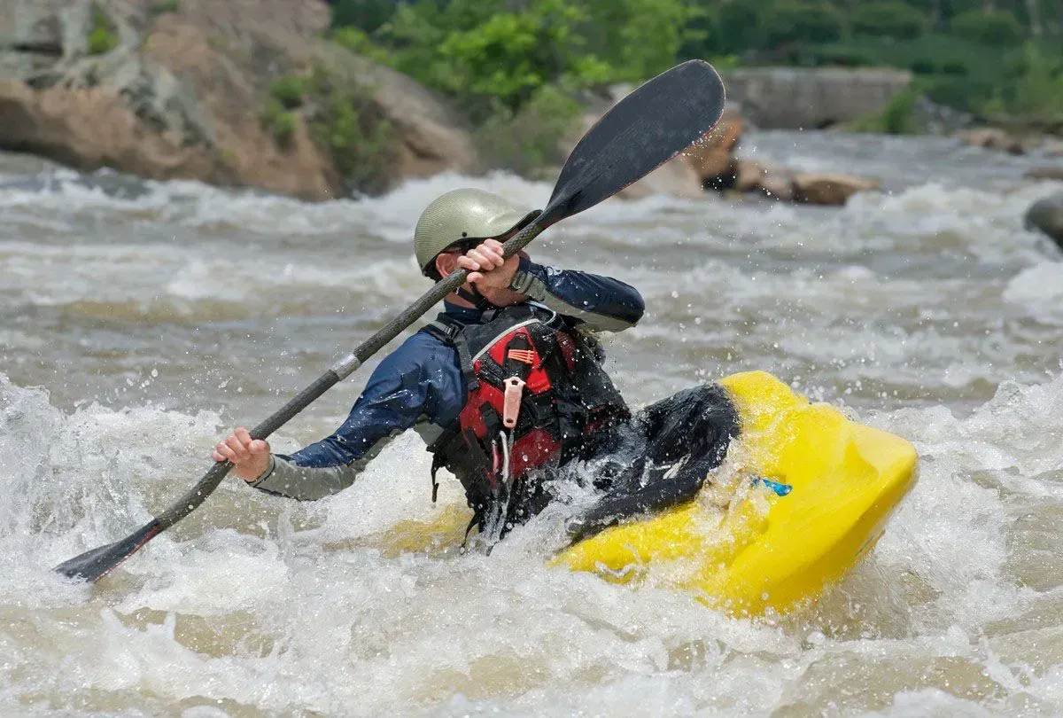 Person kayaking through rough river rapids.