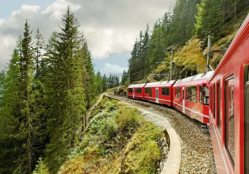Red train traveling through forested mountain landscape.