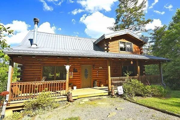 Log cabin with porch in wooded area.