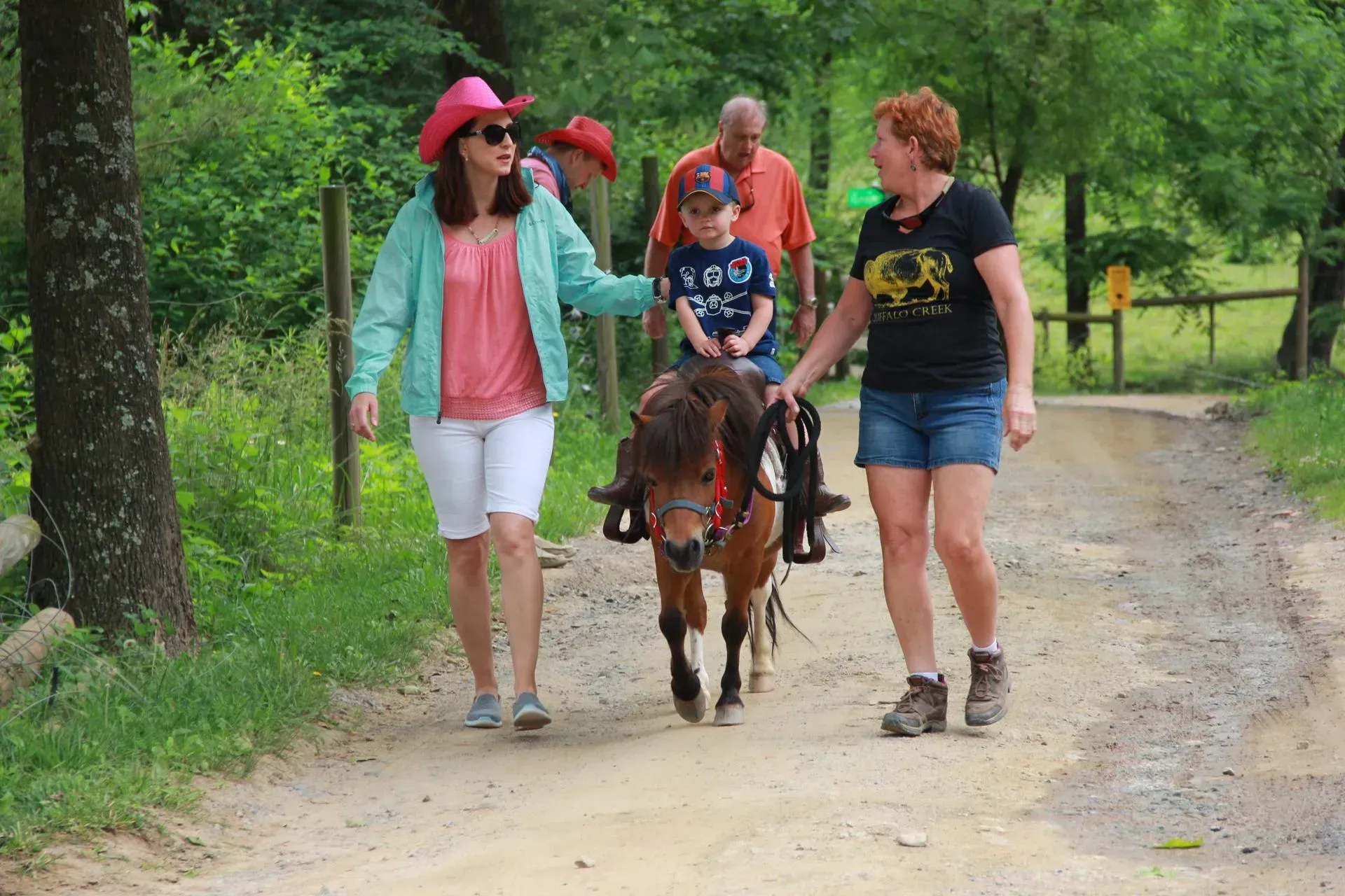 Child riding pony with adult supervision outdoors.