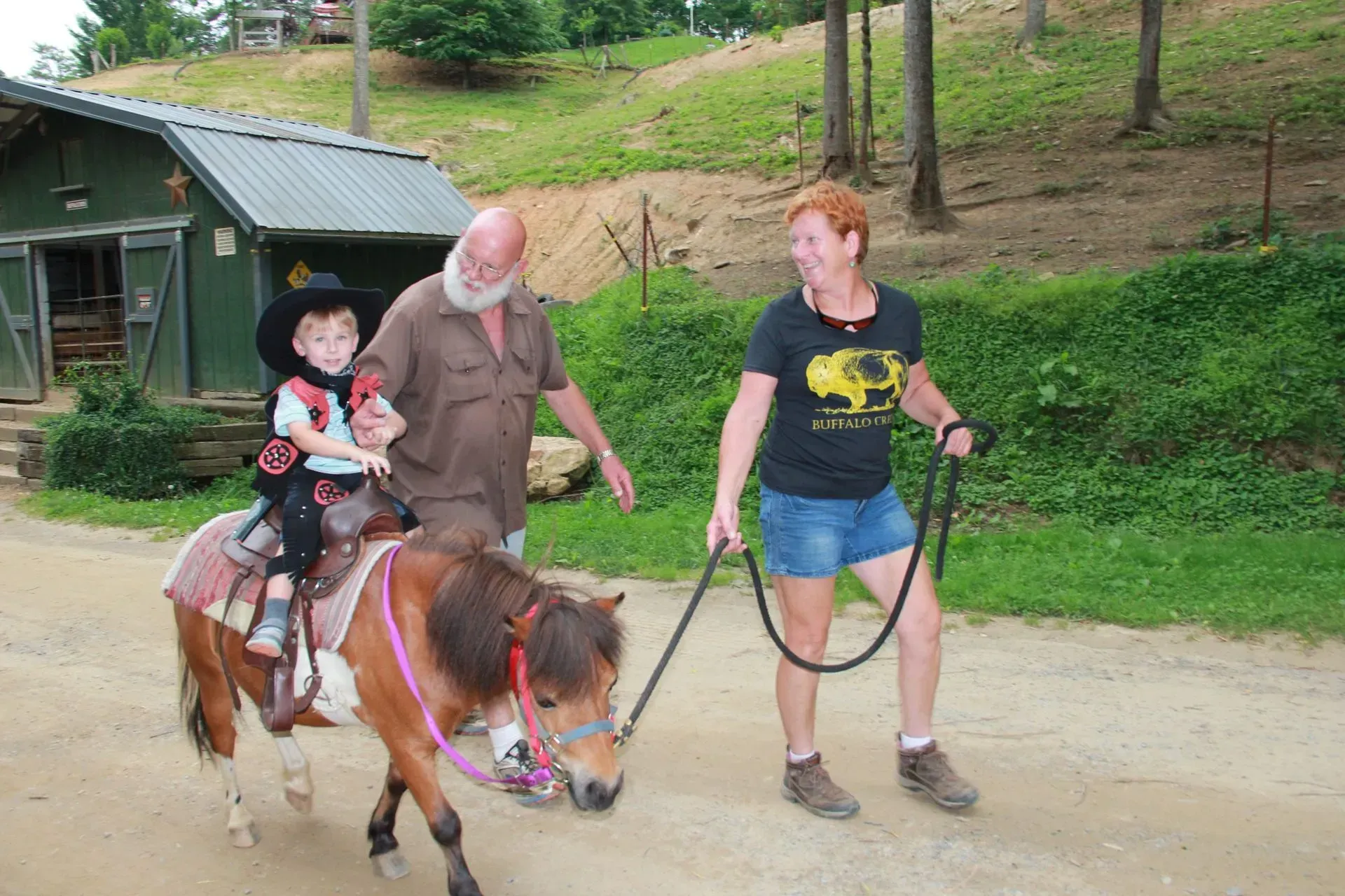 Child riding pony with adult supervision outdoors.