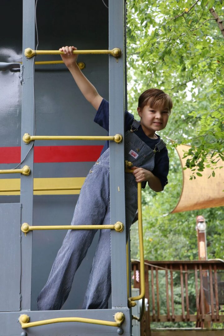 Child climbing train ladder in overalls outdoors.