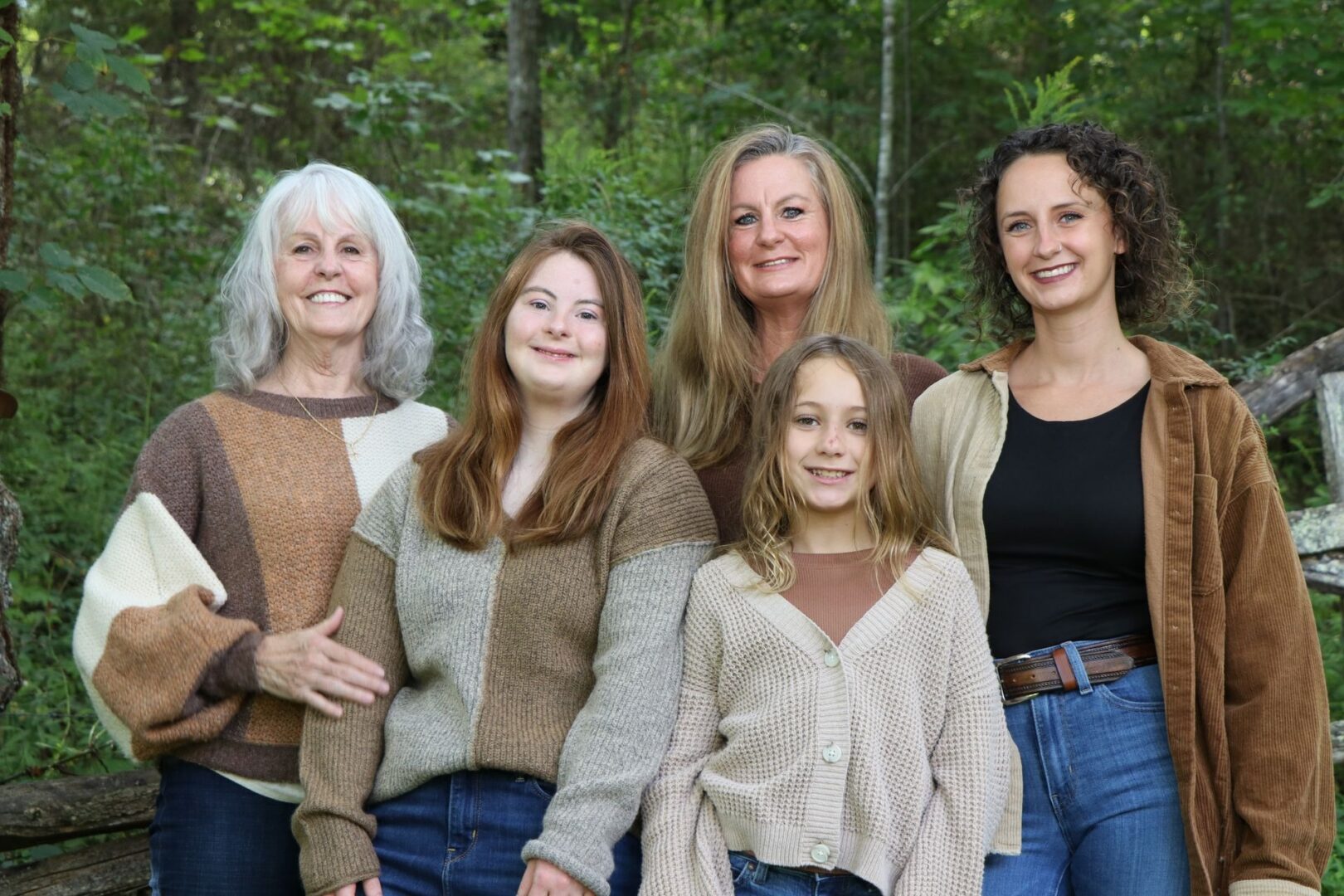 Five women smiling in a forest setting.