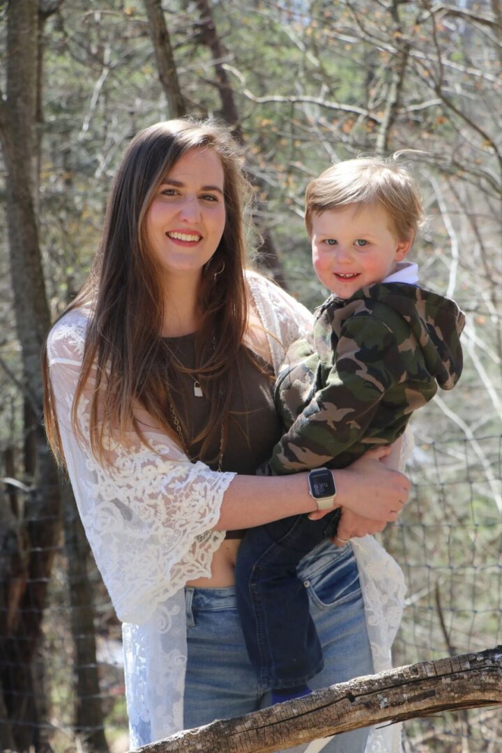 Woman holding child in outdoor setting.