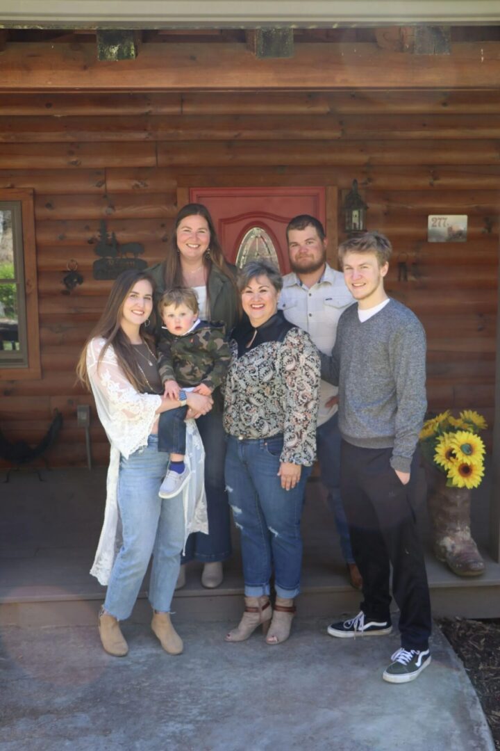 Family posing in front of wooden house.