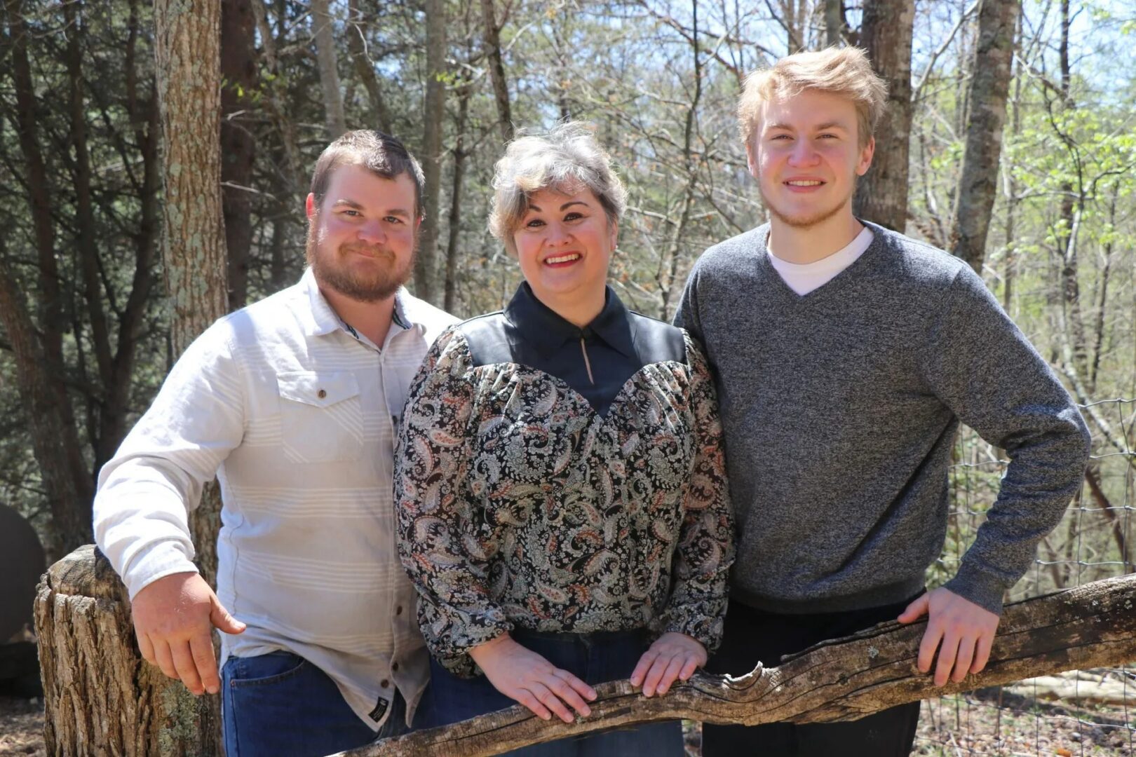 Three people posing outdoors near trees.