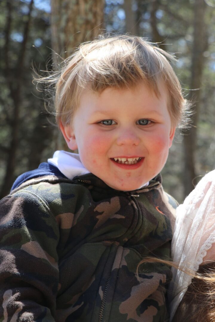 Smiling child in camouflage jacket outdoors.