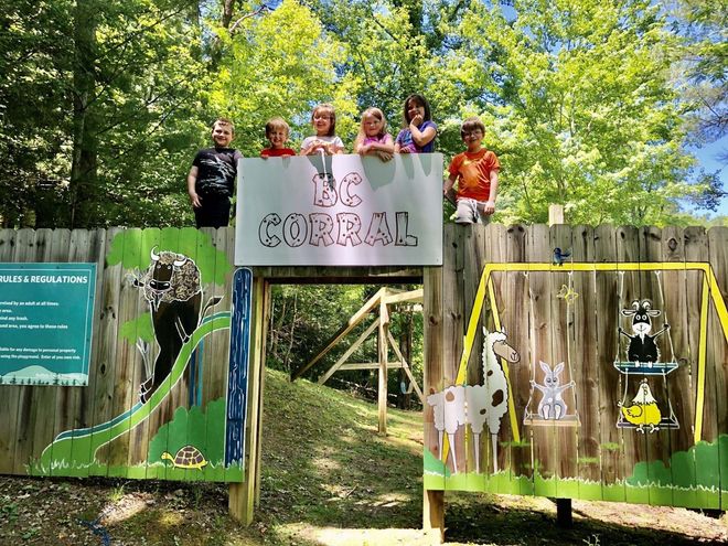 Children standing on colorful wooden fence.