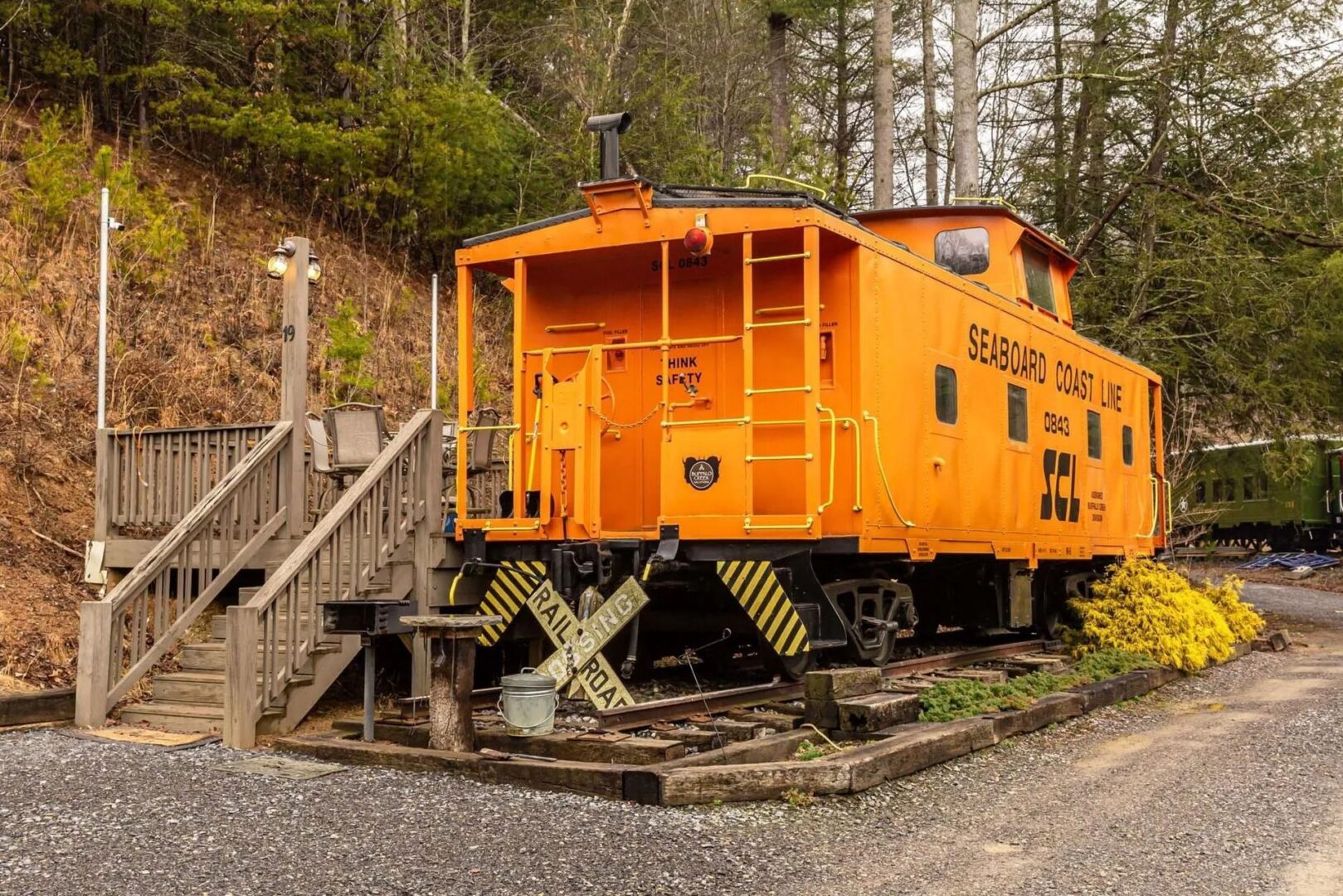 Orange train caboose with wooden stairs nearby.