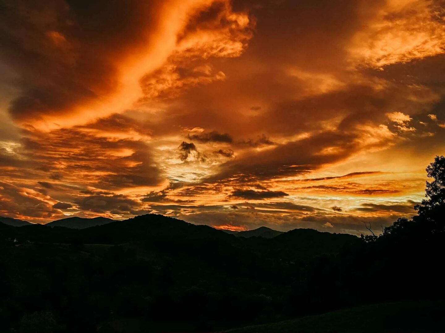 Fiery sunset over silhouetted mountain landscape.