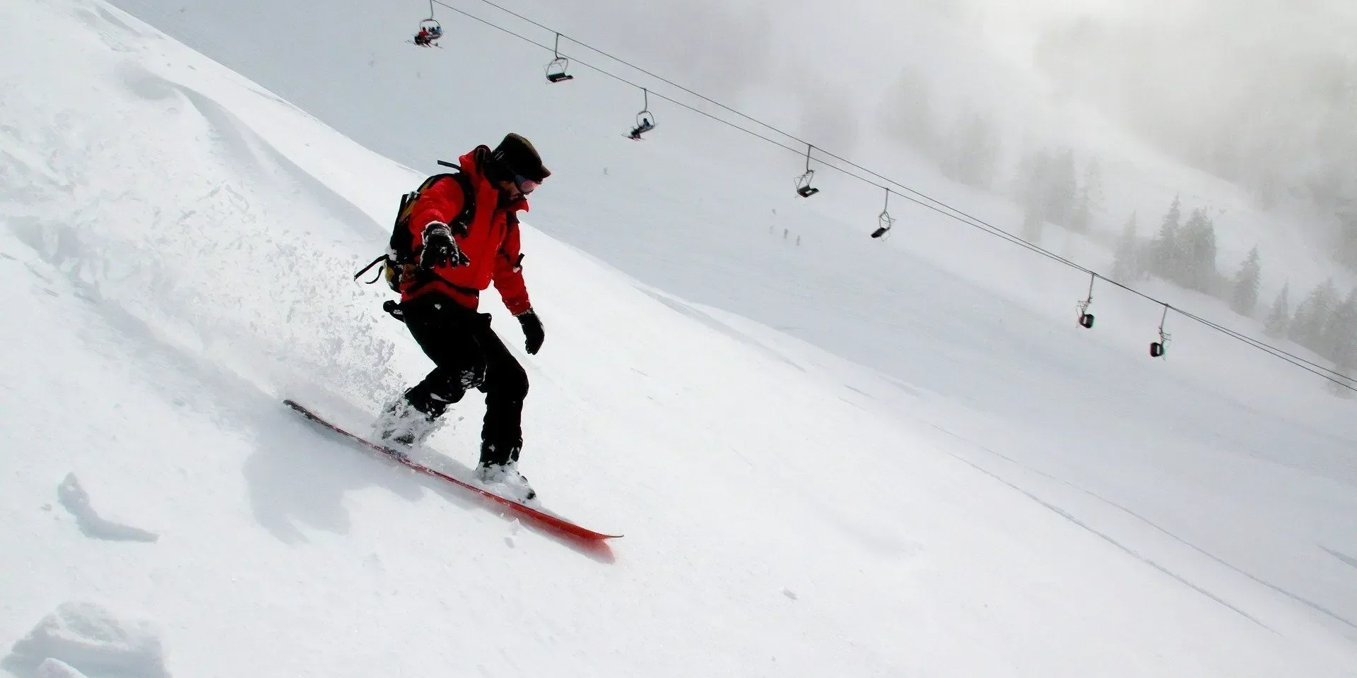 Snowboarder descending snowy mountain with ski lifts.